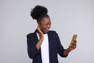 Açık gri arka planda akıllı telefon kullanan mutlu genç kadın