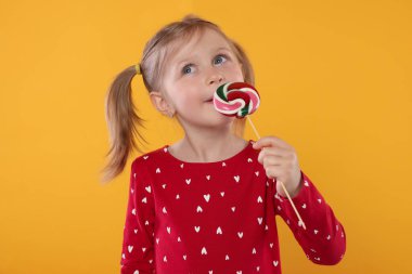 Turuncu arka planda lolipop yalayan tatlı bir kızın portresi