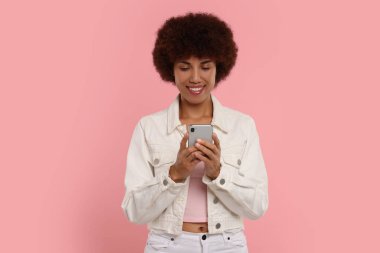 Pembe arka planda akıllı telefonu olan mutlu genç bir kadın.
