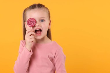 Turuncu arka planda parlak lolipop kıvrımlarıyla gözlerini kapatan duygusal küçük kız, mesaj için boşluk.