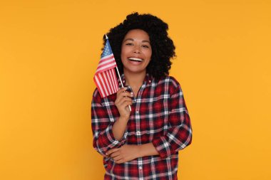 4 Temmuz - ABD 'nin Bağımsızlık Günü. Sarı arka planda Amerikan bayrağı taşıyan mutlu kadın.