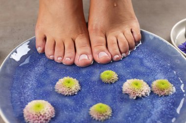 Ayaklarını tabağa su ve çiçeklerle daldıran kadın, yakın plan. Pedikür prosedürü