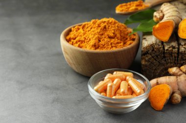 Aromatik zerdeçal tozu, kökler ve haplar gri masada. Metin için boşluk