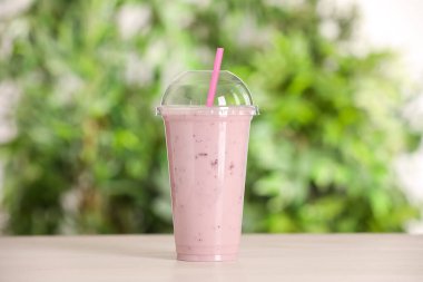 Dışarıdaki ahşap masada plastik bir bardak lezzetli smoothie.