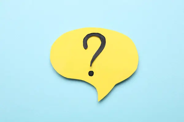 Paper speech bubble with question mark on light blue background, above view