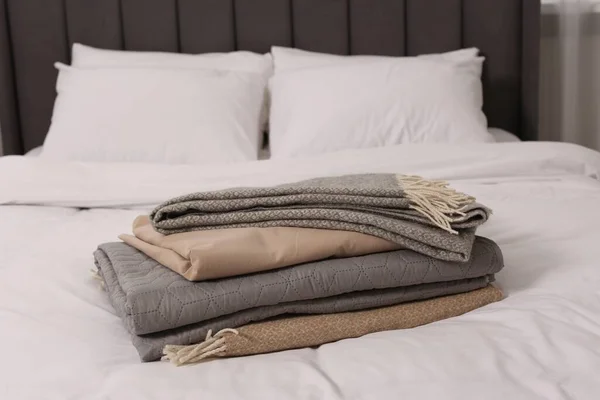 Stack of different folded blankets on bed in room. Home textile
