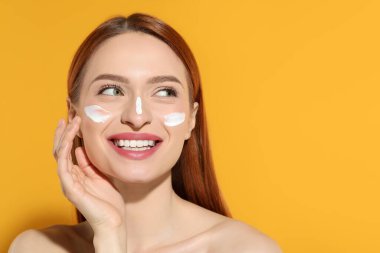 Yüzünde güneş kremi olan güzel genç bir kadın turuncu arka planda, mesaj için yer var.