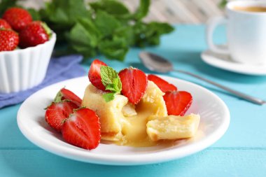 Açık mavi ahşap masada beyaz çikolatalı ve çilekli vanilyalı tatlı, yakın plan.