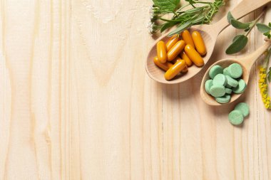 Farklı haplar, şifalı otlar ve çiçekler ahşap masada, düzlük ve yazı için yer var. Beslenme takviyeleri