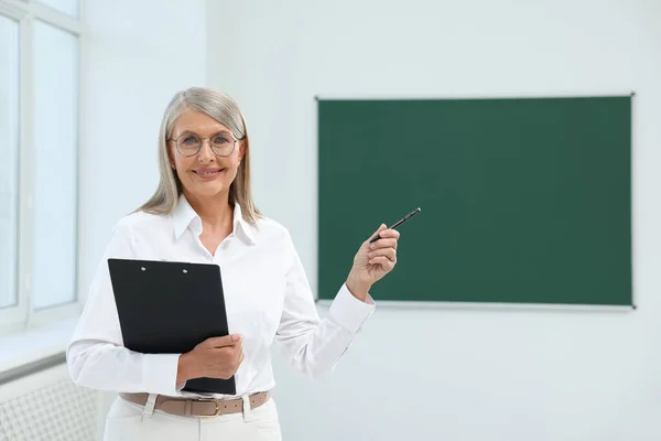 Portrait of happy professor with clipboard and pen in classroom, space for text