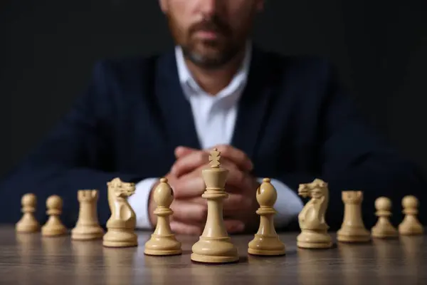 Man with chess pieces at wooden table against dark background, closeup