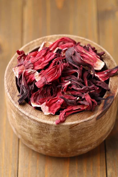 Dry hibiscus tea in bowl on wooden table, closeup