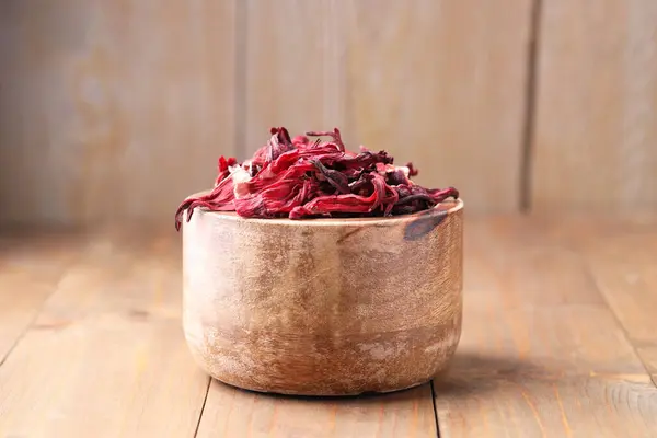 Dry hibiscus tea in bowl on wooden table
