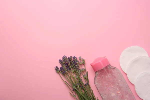 Bottle of makeup remover, cotton pads and lavender on pink background, flat lay. Space for text