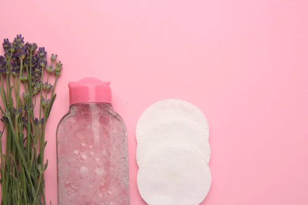 Bottle of makeup remover, cotton pads and lavender on pink background, flat lay. Space for text
