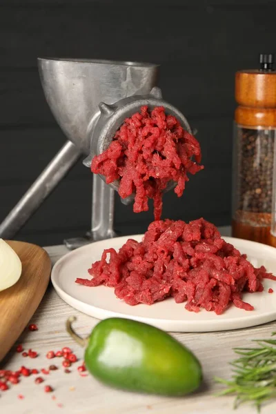 Metal meat grinder with minced beef on light wooden table