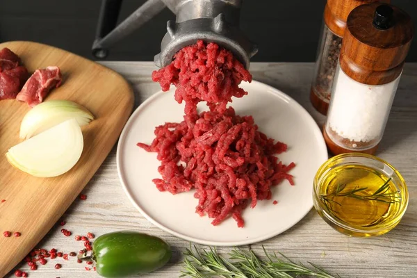 Metal meat grinder with minced beef and spices on light wooden table