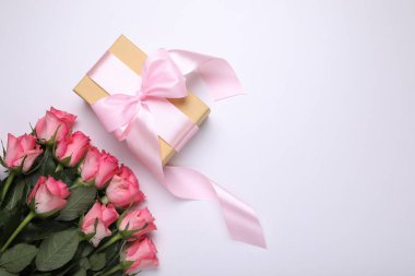 Pembe fiyonklu hediye kutusu ve beyaz arka planda güzel çiçekler, düz bir zemin. Metin için boşluk