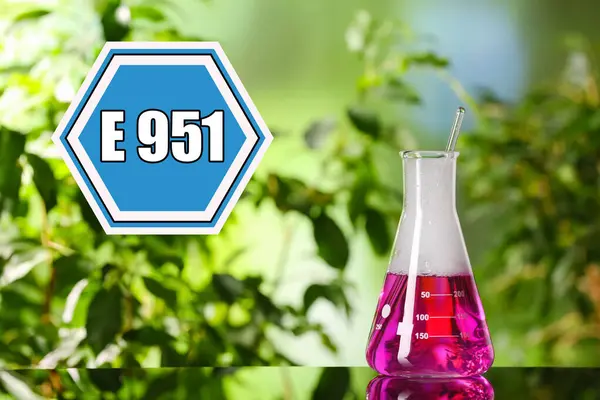 Information about artificial sweetener in product. Blue sign with aspartame code (E951) and flask with liquid on table outdoors