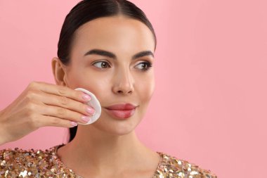 Güzel bir kadın pembe arka planda pamuklu ped ile makyajı kaldırıyor. Metin için boşluk
