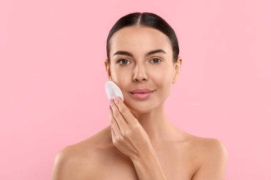 Güzel bir kadın pembe arka planda pamukla makyajı kaldırıyor.