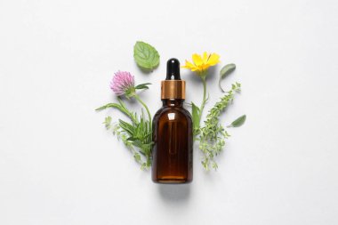 Temel yağ şişesi, beyaz arka planda farklı otlar ve çiçekler, düz bir zemin.