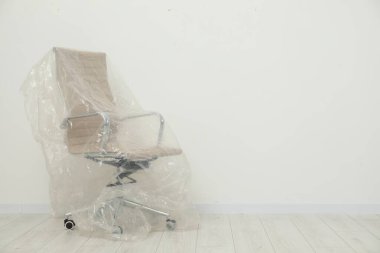 Beyaz duvarın yanındaki plastik filmle kaplı modern ofis koltuğu. Metin için boşluk