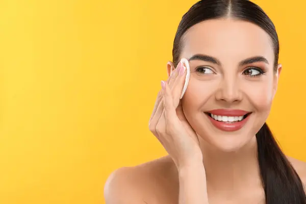 stock image Beautiful woman removing makeup with cotton pad on orange background, space for text