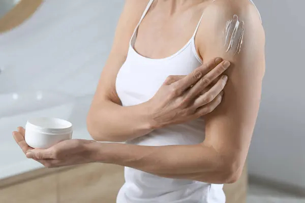 Woman applying body cream onto arm in bathroom, closeup