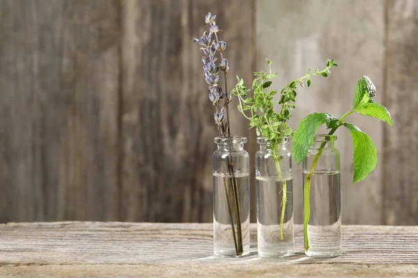 Bottles with essential oils and plants on wooden table. Space for text