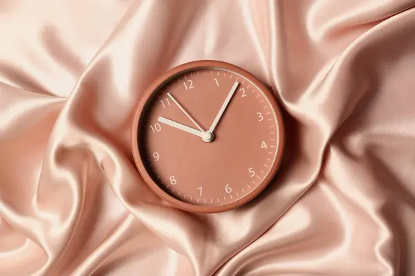 One stylish clock on beige cloth, top view