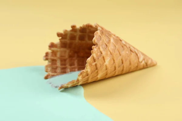 Melted ice cream and wafer cone on beige background, closeup