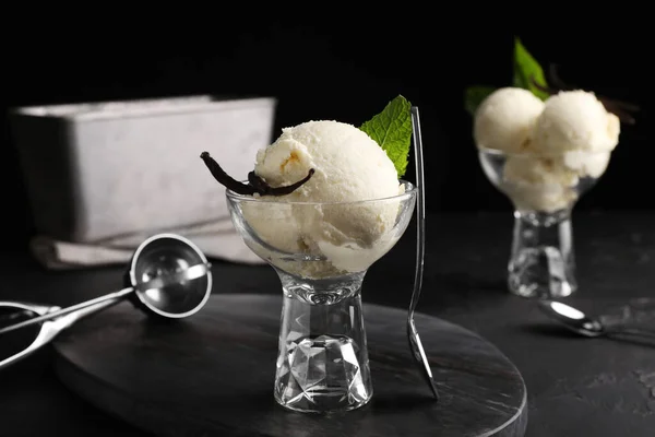 Tasty ice cream with vanilla pods in glass dessert bowl on black table
