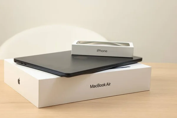 stock image Leiden, Netherlands - October 6, 2023: Modern black MacBook Air and box from iPhone 15 Pro Max on wooden table