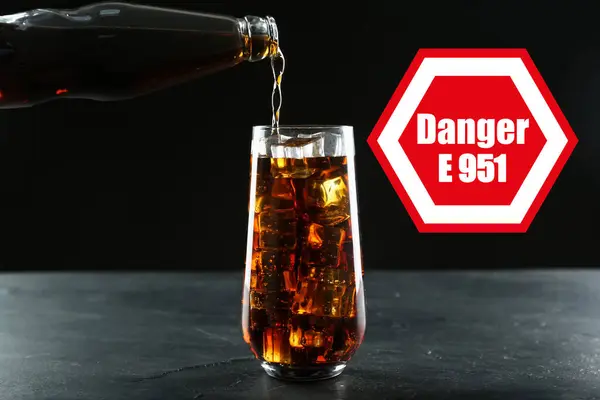 Caution about using of aspartame in product. Warning sign with artificial sweetener code (E951) and word Danger. Pouring soda drink containing sugar substitute against black background