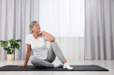 Evde paspasın üzerinde oturan mutlu yaşlı kadın, mesaj için yer var. Yoga alıştırması.
