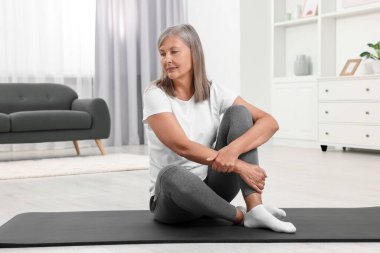 Evde paspasın üzerinde oturan yaşlı kadın. Yoga alıştırması.