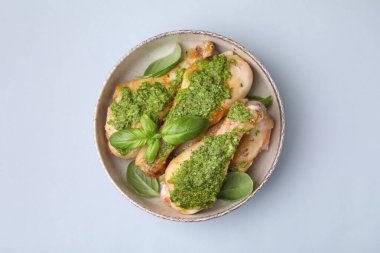 Pesto soslu tavuk budu ve açık gri masada fesleğen.