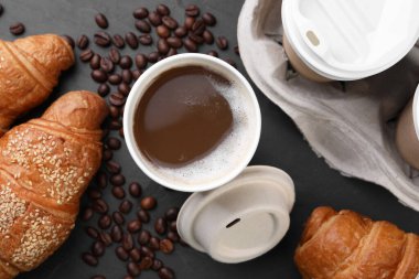 Paket kahve. Lezzetli içeceklerle dolu kağıt bardaklar, kruvasan ve fasulyeler siyah masada, düz uzanmış.