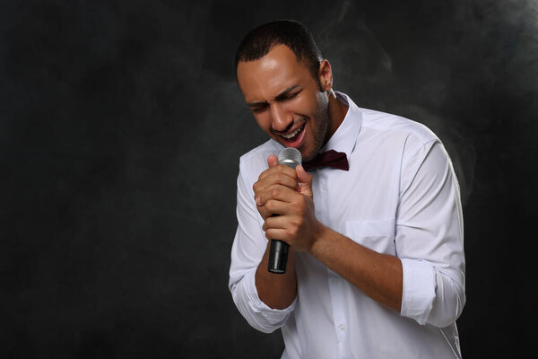 Handsome man with microphone singing on black background. Space for text