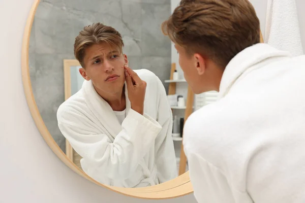 鏡を見つめている若い男は 屋内で顔にピンプルに触れました アクネ問題 — ストック写真