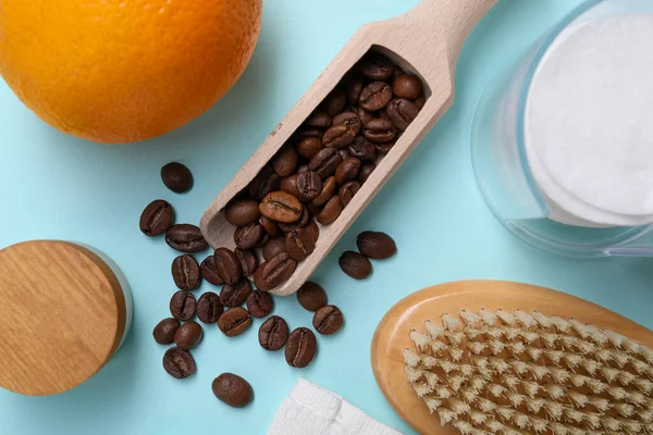 Coffee beans, orange and brush on light blue background, flat lay. Anti cellulite treatment