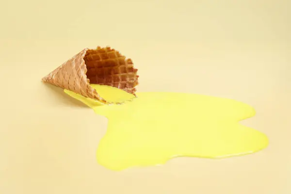 Melted ice cream and wafer cone on yellow background