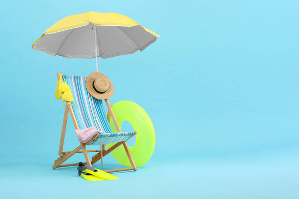 Deck chair, umbrella and beach accessories against light blue background, space for text. Summer vacation