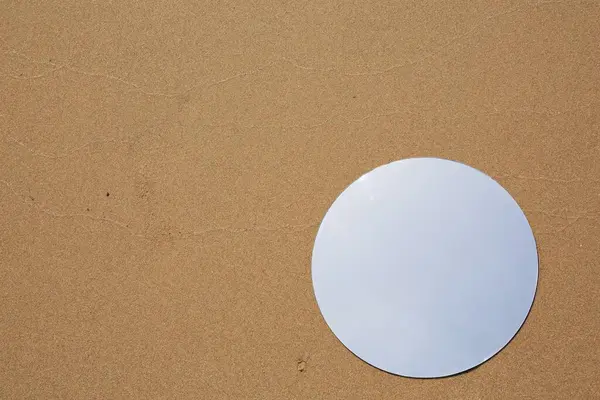 Round mirror reflecting sky on sand outdoors, top view. Space for text