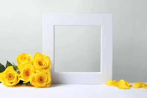 Beautiful presentation for product. Frame and yellow roses on white table against light grey background, space for text