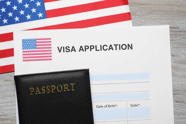 Immigration to USA. Visa application form, passport and flag on light wooden table, flat lay