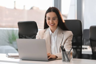 Ofisteki beyaz masada modern laptop kullanan mutlu kadın.