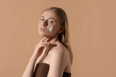 Yüzünde bej arka planda güneş kremi olan güzel genç bir kadın. Mesaj için yer var.