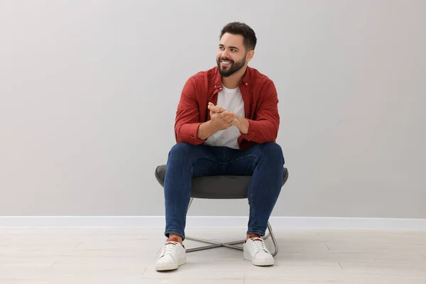 Handsome man sitting in armchair near light grey wall indoors